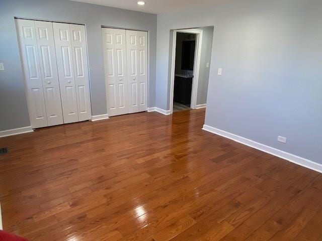 unfurnished bedroom featuring multiple closets and dark wood-type flooring