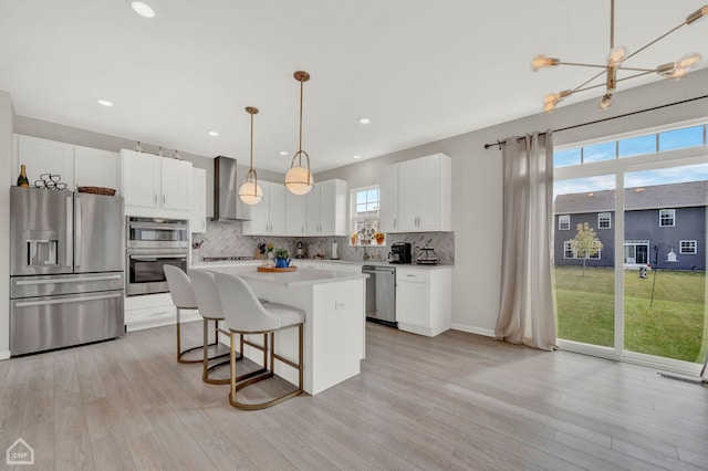 kitchen featuring white cabinetry, stainless steel appliances, a kitchen island, wall chimney exhaust hood, and pendant lighting