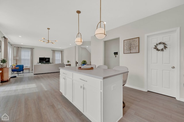 kitchen with a breakfast bar, a center island, light wood-type flooring, white cabinets, and hanging light fixtures