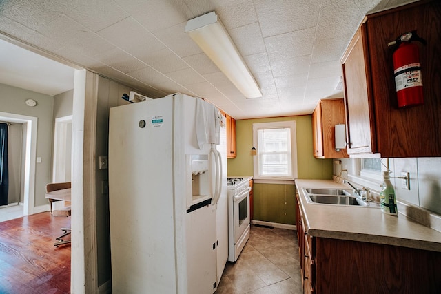 kitchen featuring brown cabinets, white appliances, light countertops, and a sink