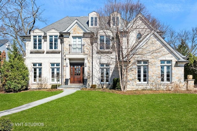 french country home with french doors, stone siding, a front lawn, and a balcony