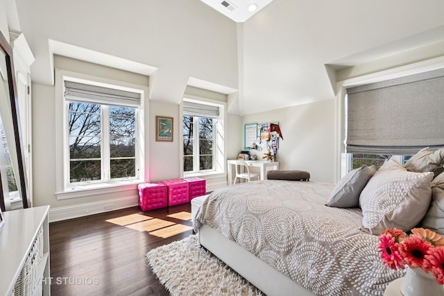 bedroom with visible vents, baseboards, a towering ceiling, and wood finished floors