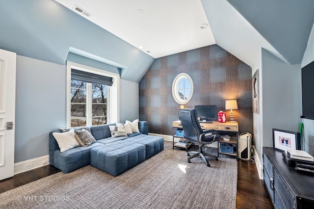 home office with dark wood-type flooring, an accent wall, vaulted ceiling, wallpapered walls, and baseboards