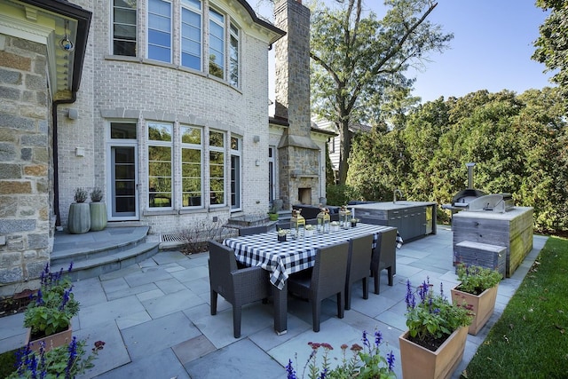 view of patio / terrace with a hot tub, outdoor dining area, and an outdoor stone fireplace