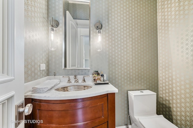 bathroom with toilet, wallpapered walls, and vanity