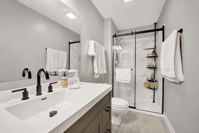 bathroom featuring baseboards, toilet, vanity, and a marble finish shower