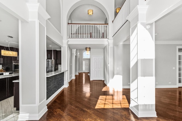 entrance foyer featuring dark wood-type flooring, baseboards, crown molding, and a high ceiling