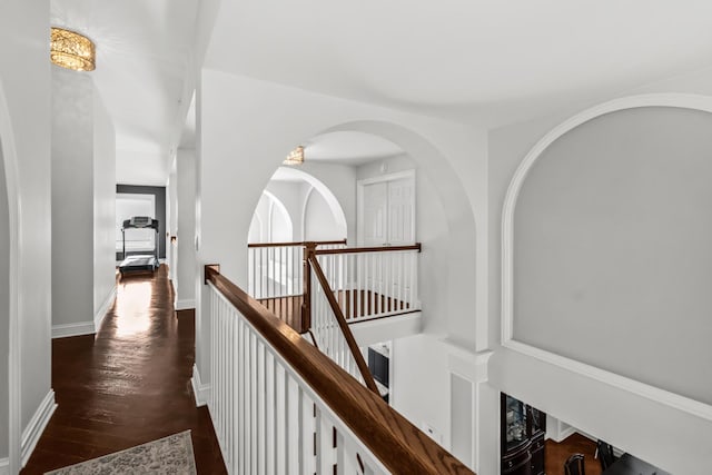 corridor with dark wood-style flooring, an upstairs landing, and baseboards