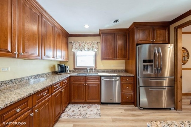 kitchen featuring visible vents, appliances with stainless steel finishes, a sink, light stone countertops, and light wood-type flooring