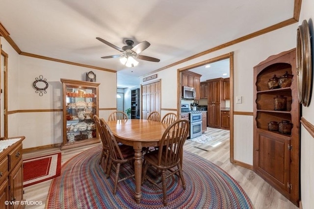 dining space featuring light wood-type flooring, a wainscoted wall, a ceiling fan, and crown molding