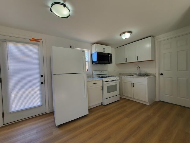 kitchen featuring white appliances, white cabinets, a sink, and wood finished floors