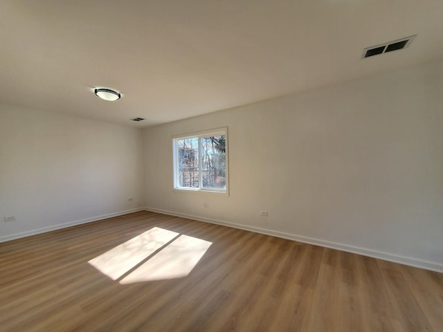 spare room featuring baseboards, visible vents, and wood finished floors