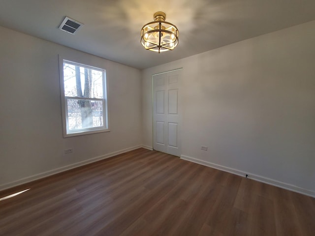 empty room with visible vents, dark wood finished floors, baseboards, and an inviting chandelier