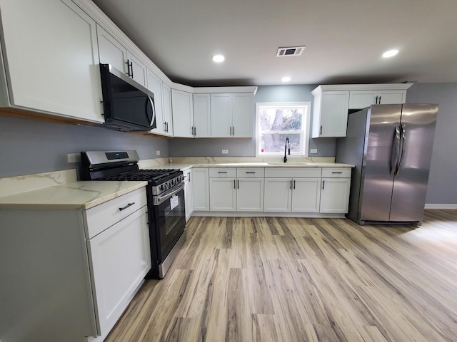 kitchen with visible vents, appliances with stainless steel finishes, light wood-type flooring, white cabinetry, and a sink