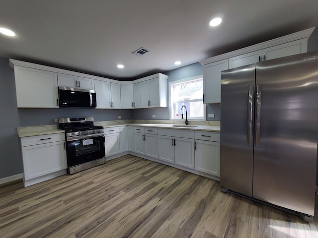 kitchen featuring light wood finished floors, stainless steel appliances, recessed lighting, visible vents, and a sink