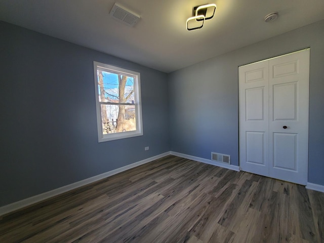 unfurnished bedroom featuring a closet, visible vents, dark wood finished floors, and baseboards