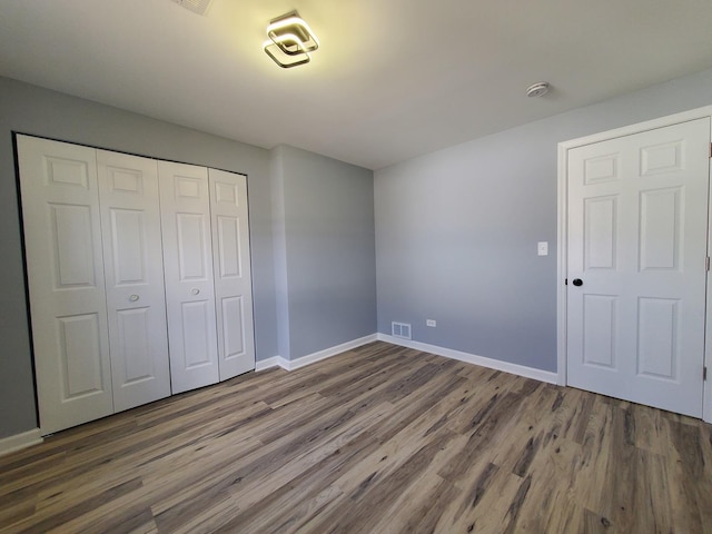 unfurnished bedroom featuring a closet, visible vents, baseboards, and wood finished floors