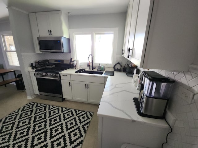 kitchen featuring light stone counters, stainless steel appliances, a sink, white cabinetry, and tasteful backsplash