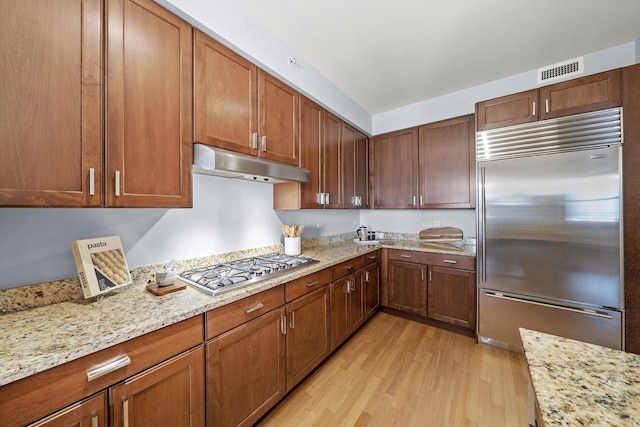 kitchen featuring light stone counters, under cabinet range hood, visible vents, light wood-style floors, and appliances with stainless steel finishes