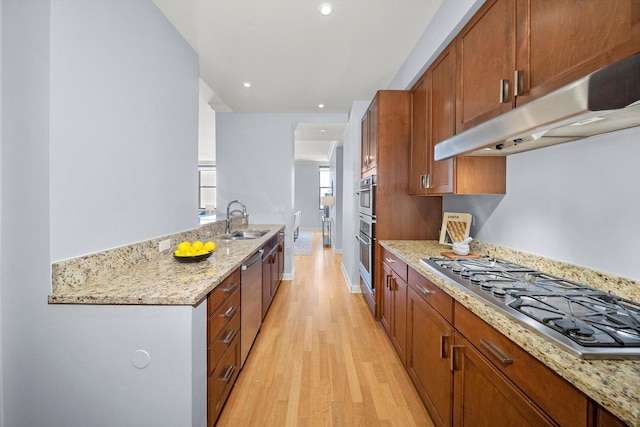 kitchen featuring light wood-style flooring, appliances with stainless steel finishes, light stone counters, under cabinet range hood, and a sink