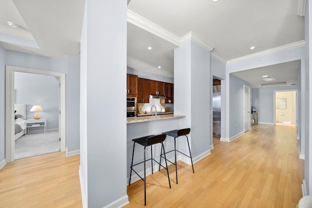 kitchen with baseboards, a breakfast bar area, ornamental molding, light wood-type flooring, and under cabinet range hood