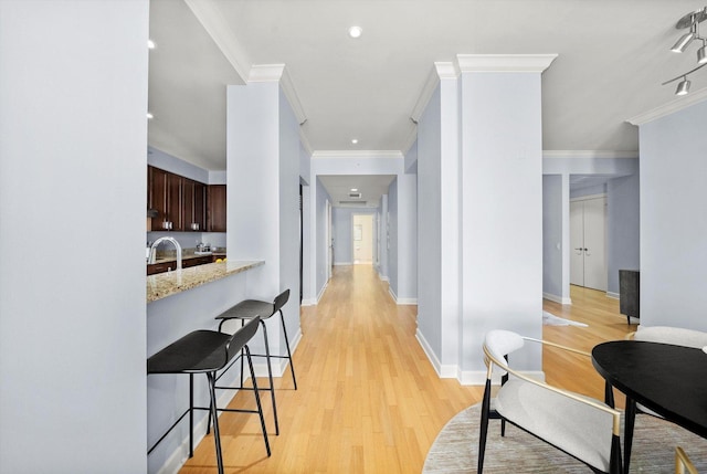 hallway with a sink, light wood-style floors, baseboards, and crown molding