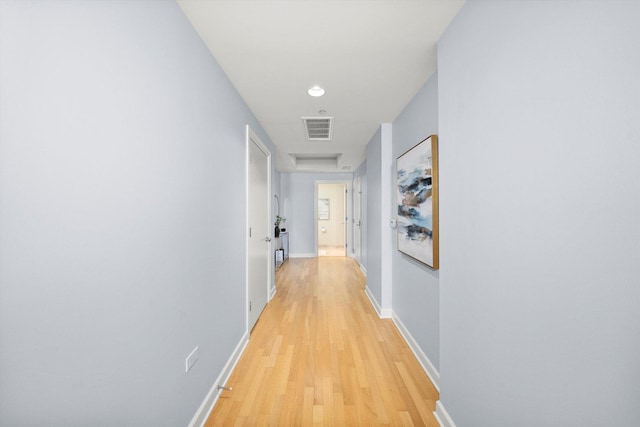 corridor with attic access, visible vents, light wood-style flooring, and baseboards