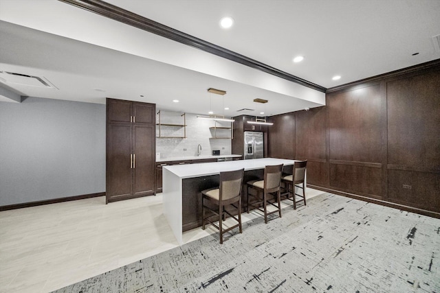 kitchen featuring crown molding, a breakfast bar area, light countertops, dark brown cabinetry, and stainless steel fridge