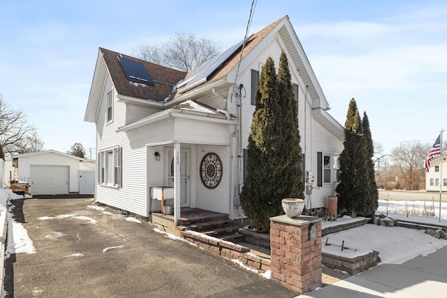 view of front of home featuring a shingled roof, roof mounted solar panels, a garage, an outdoor structure, and driveway