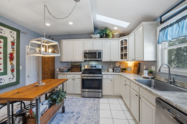 kitchen featuring pendant lighting, stainless steel appliances, glass insert cabinets, white cabinetry, and a sink