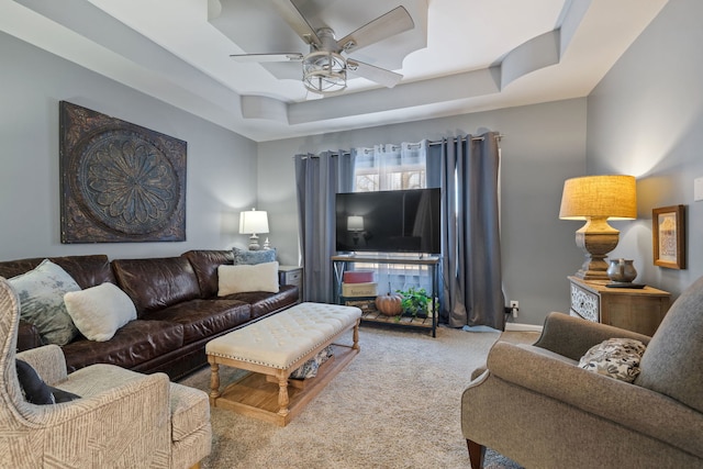 carpeted living room with a tray ceiling, ceiling fan, and baseboards