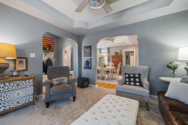 living area featuring arched walkways, a raised ceiling, a ceiling fan, and baseboards