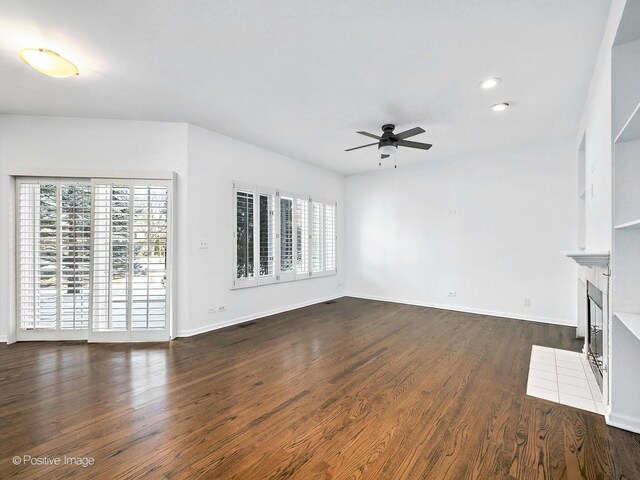 unfurnished living room with ceiling fan, dark wood-type flooring, a tiled fireplace, and baseboards