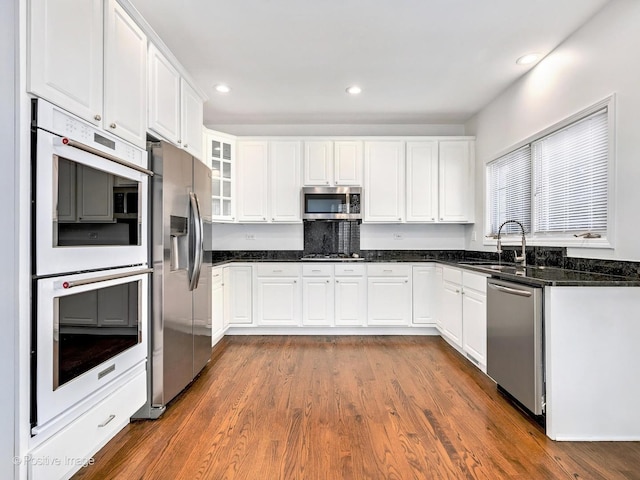 kitchen with appliances with stainless steel finishes, white cabinetry, glass insert cabinets, and a sink