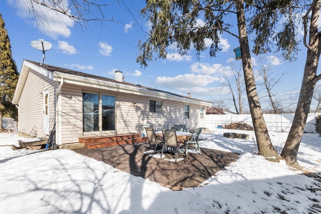 snow covered house featuring entry steps, a chimney, and fence