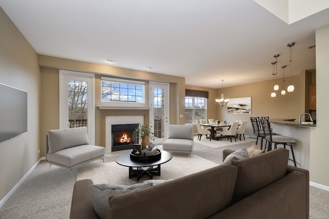 living room with a tiled fireplace, carpet flooring, an inviting chandelier, and baseboards