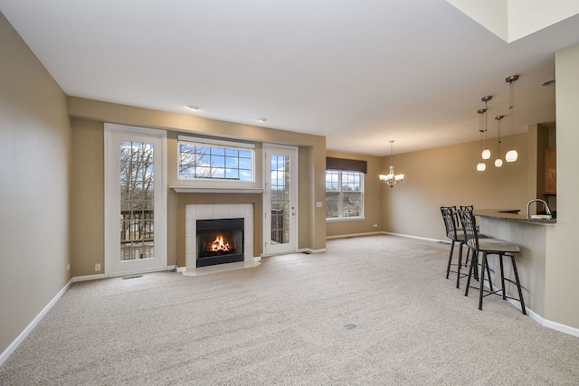 living room with light carpet, visible vents, baseboards, a tile fireplace, and an inviting chandelier