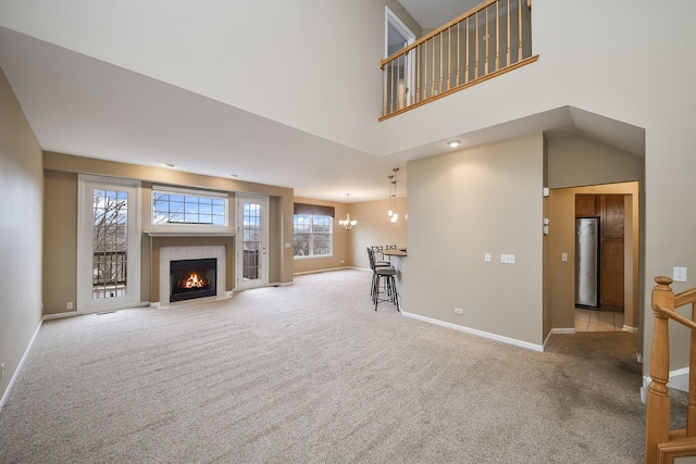 unfurnished living room featuring a chandelier, carpet, a high ceiling, baseboards, and a tiled fireplace