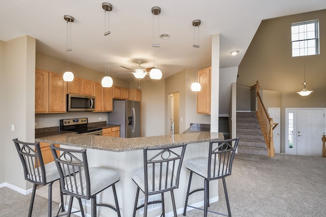 kitchen featuring baseboards, light colored carpet, appliances with stainless steel finishes, a peninsula, and a kitchen bar