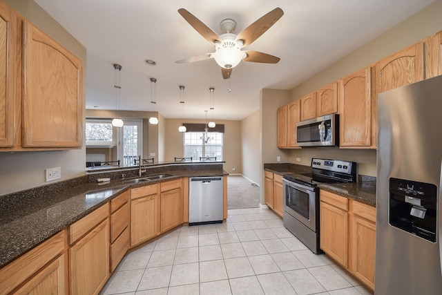 kitchen featuring light tile patterned flooring, a peninsula, a sink, appliances with stainless steel finishes, and decorative light fixtures