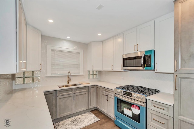 kitchen with light wood-type flooring, stainless steel appliances, sink, light stone counters, and white cabinets