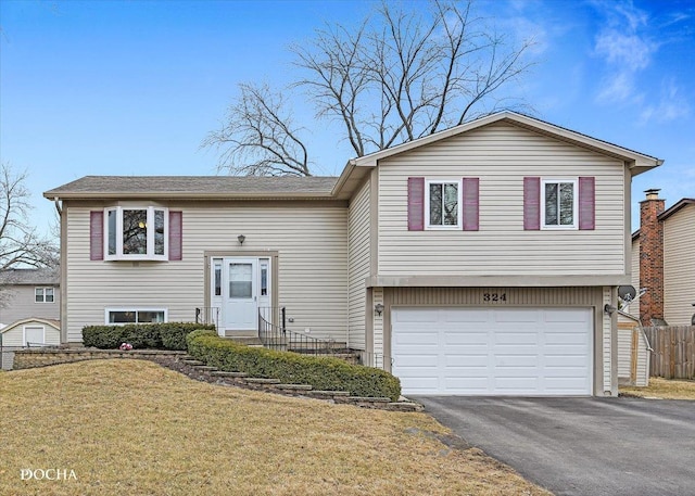 bi-level home with a garage, a front lawn, fence, and aphalt driveway