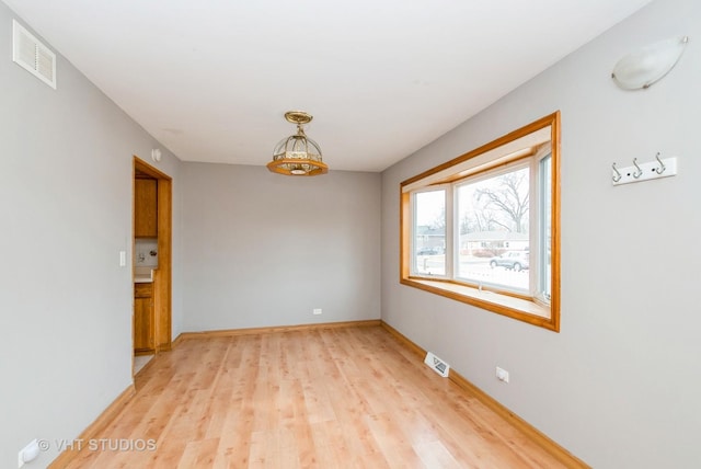 empty room featuring light wood-style floors, visible vents, and baseboards