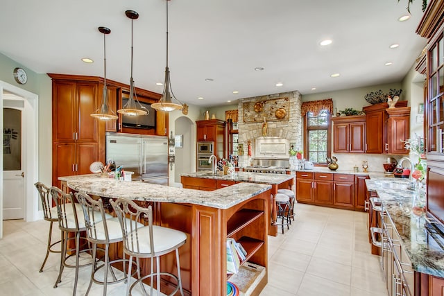 kitchen featuring built in appliances, light stone counters, decorative light fixtures, a large island, and tasteful backsplash