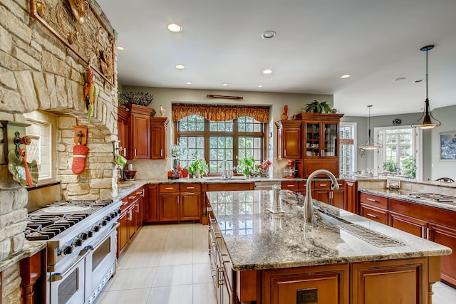 kitchen featuring appliances with stainless steel finishes, sink, light stone counters, pendant lighting, and an island with sink