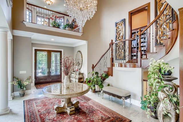 entryway featuring an inviting chandelier, french doors, a towering ceiling, ornamental molding, and ornate columns