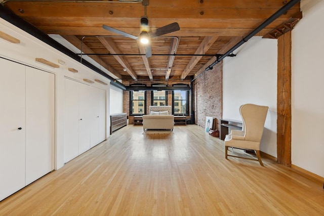 unfurnished room featuring a ceiling fan, wooden ceiling, brick wall, light wood-type flooring, and beam ceiling