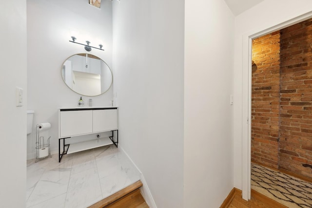 bathroom featuring marble finish floor, brick wall, baseboards, and vanity