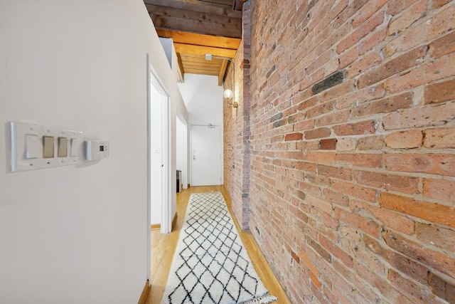 hallway with light wood finished floors, brick wall, and beamed ceiling