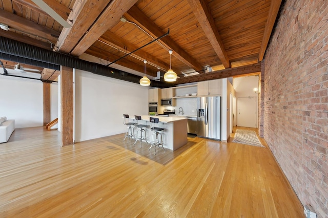 kitchen featuring light wood finished floors, brick wall, a breakfast bar area, stainless steel appliances, and white cabinetry